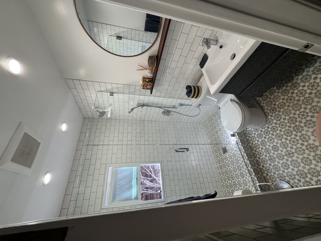 Full bathroom with glass-enclosed walk-in shower, tiled floor and round mirror